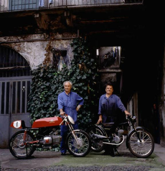 Officina di moto d'epoca - meccanici in posa accanto a una motocicletta nel cortile