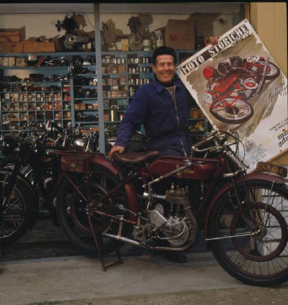 Moto officina - il titolare posa accanto a una moto d'epoca mostrando un poster