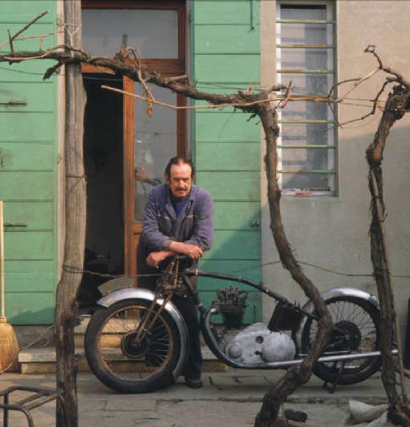 Meccanico posa accanto al telaio di una moto d'epoca nel cortile