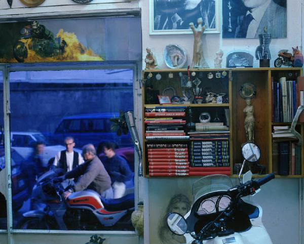 Interno - Scaffale con soprammobili e libri per moto - Dalla finestra si intravvedono alcuni appassionati di moto