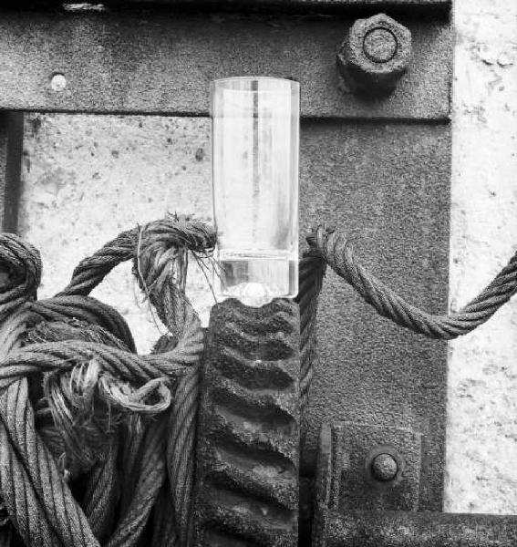 Stll - life con bicchiere appoggiato su di un ingranaggio - attorno cavi metallici