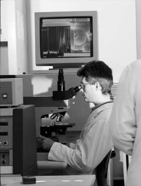 Glaxo - Ricercatore in camice bianco al microscopio - sullo sfondo uno schermo con encefalogramma