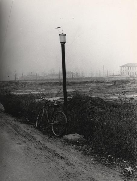 Milano - Quartiere Gratosoglio - Bicicletta appoggiata a un lampione su  una strada sterrata - Terreno incolto