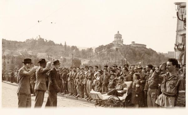 Torino - Sfilata per la Liberazione - Il generale Alessandro Trabucchi, Francesco Scotti e un compagno salutano un drappello di partigiani schierati lungo la strada - Uomo ferito su barella