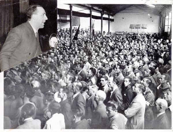 Francesco Scotti parla a una assemblea di lavoratori - Interno di fabbrica - Bandiere - Cartelli - Fotomontaggio