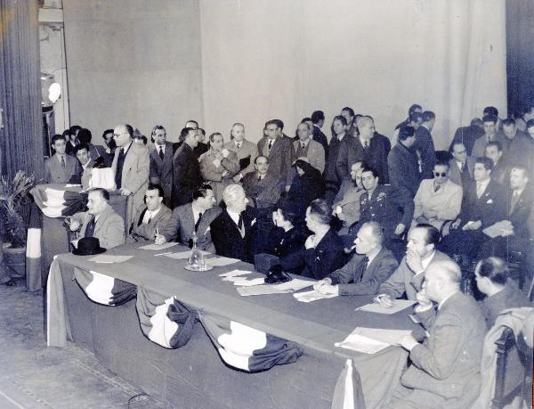 Roma - Teatro Italia - Primo Congresso della Resistenza italiana - Francesco Scotti (sullo sfondo di profilo) accanto ad altri compagni - Tavolo dei delegati - Palco con oratore - Bandiere