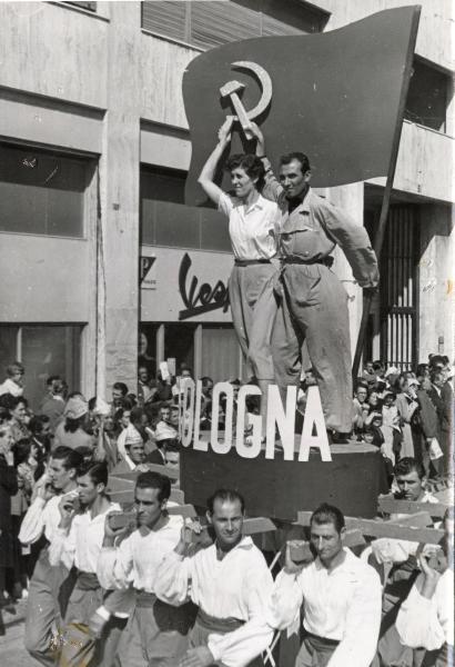 Genova - Festa nazionale de l'Unità 1950 - Sfilata per le vie della città - Spezzone di corteo con la rappresentanza di Bologna - Gruppo di uomini trasporta una pedana con due operai che reggono il simbolo della falce e martello - Bandiera