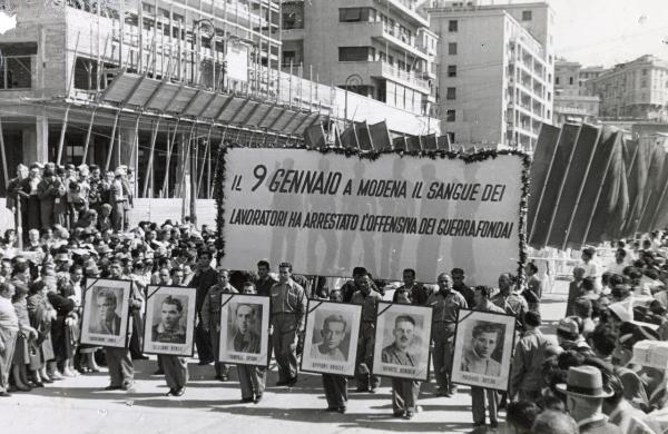 Genova - Festa nazionale de l'Unità 1950 - Sfilata per le vie della città - Spezzone di corteo con lo striscione che ricorda l'eccidio delle Fonderie Riunite di Modena - Ritratti degli operai morti listati a lutto - Bandiere