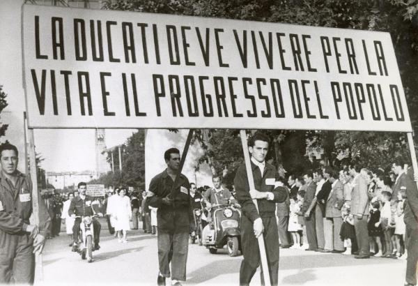 Bologna - Festa provinciale de l'Unità 1953 - Sfilata per le vie della città - Spezzone di corteo con gli operai della Ducati che portano un cartello - Motociclette