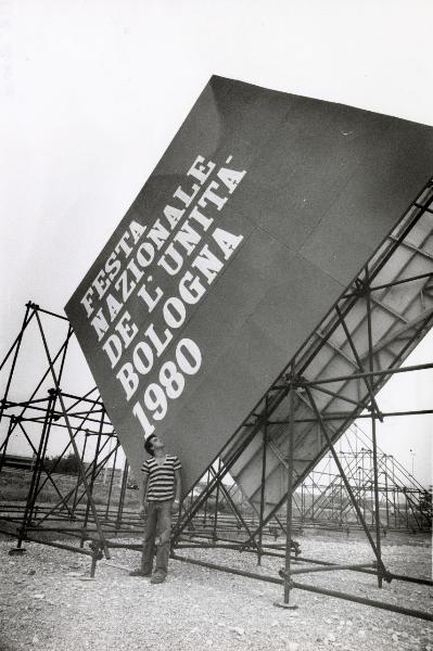 Bologna - Festa nazionale de l'Unità 1980 - Allestimento delle strutture - Un uomo osserva la grande impalcatura in metallo che sorregge il cartellone dell'ingresso - Scritte