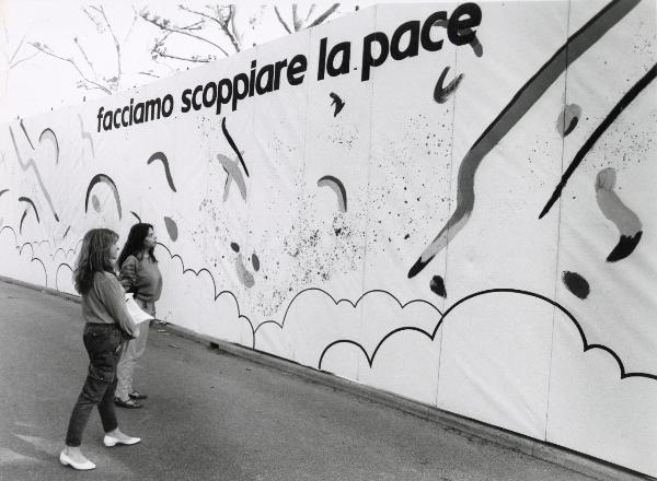 Bologna - Festa nazionale de l’Unità delle Donne 1982 - Due ragazze osservano un grande pannello con la scritta "facciamo scoppiare la pace"