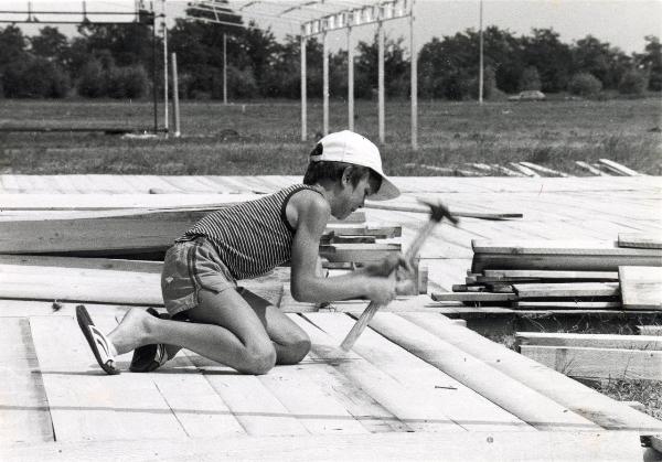 Reggio nell'Emilia - Festa nazionale de l'Unità 1983 - Allestimento degli stand - Bambino pianta un chiodo in una struttura di legno - Ritratto infantile