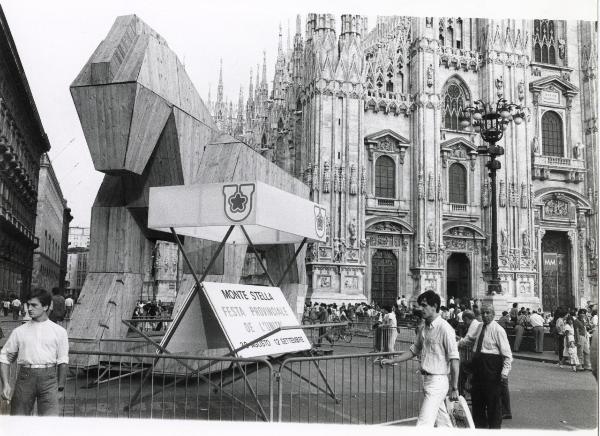 Milano - Festa provinciale de l'Unità 1983 - Piazza del Duomo - Grande installazione in legno a forma di cavallo - Struttura metallica con cartelli recanti la pubblicità della festa al Monte Stella - Folla - Facciata del Duomo