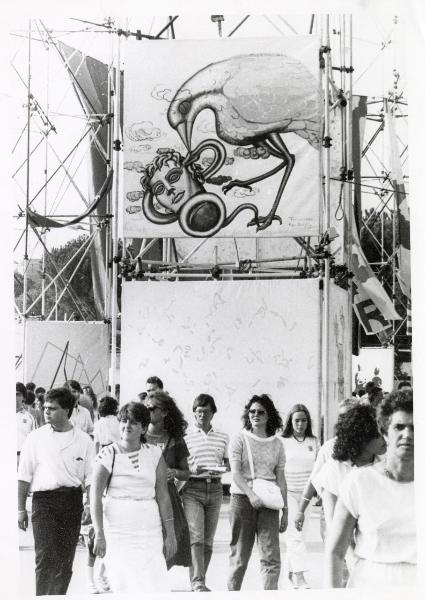 Roma - Festa nazionale de l'Unità 1984 - EUR - Folla a passeggio nella Galleria della Pace - Grande pannello che raffigura una colomba che mangia un serpente avvolto intorno alla testa di Medusa - Bandiere