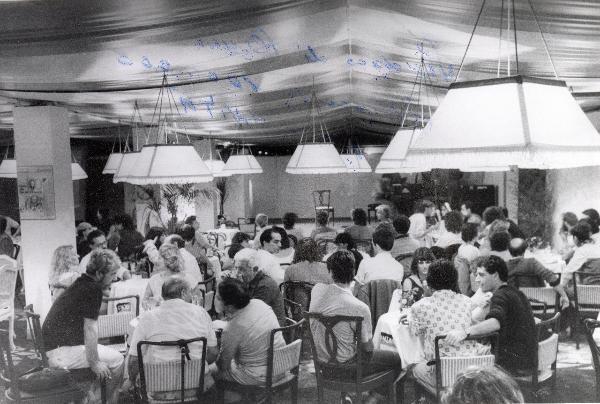 Roma - Festa nazionale de l'Unità 1984 - EUR - Il caffè letterario - Palcoscenico - Pubblico riunito intorno a dei tavoli - Illuminazione