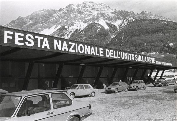 Bormio - VI Festa nazionale de l'Unità sulla neve 1984 - Grande struttura di accoglienza con insegna - Automobili - Paesaggio montano