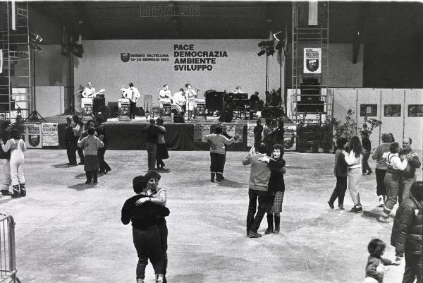 Bormio - VII Festa nazionale de l'Unità sulla neve 1985 - Serata danzante - Gruppo musicale sul palcoscenico - Cantante al microfono - Cartelli