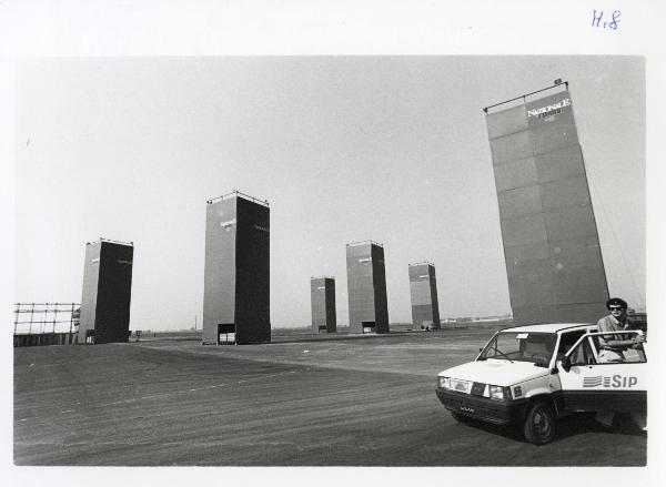 Ferrara - Festa nazionale de l'Unità 1985 - Aeroporto militare - Scorcio delle torri poste all'ingresso - Automobile - Scritte - Strutture metalliche