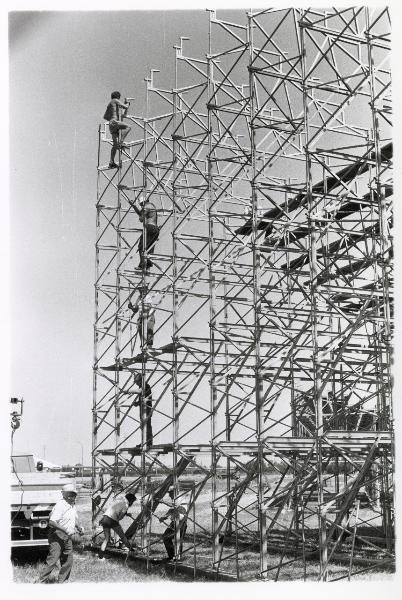 Ferrara - Festa nazionale de l'Unità 1985 - Aeroporto militare - Costruzione di una delle gradinate dell'Arena spettacoli - Operai al lavoro sopra una grande struttura metallica - Mezzi di trasporto