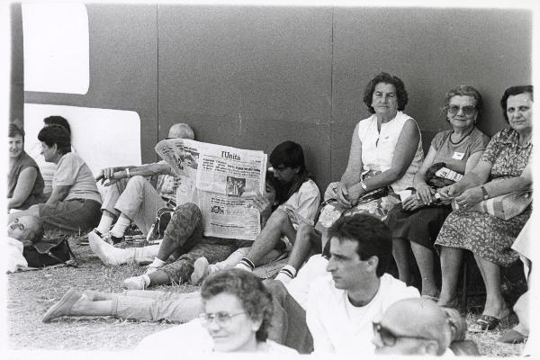 Ferrara - Festa nazionale de l'Unità 1985 - Aeroporto militare - Folla - Gruppi di persone si riposano - Giovani seduti a terra leggono una copia del giornale - Ritratto di gruppo