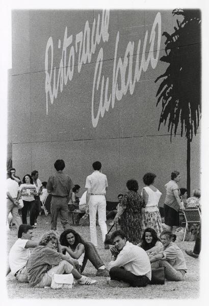 Ferrara - Festa nazionale de l'Unità 1985 - Aeroporto militare - Folla - Gruppo di di giovani seduti a terra - Gruppi di persone riunite intorno a dei tavolini - Ritratto di gruppo - Stand - Scritte