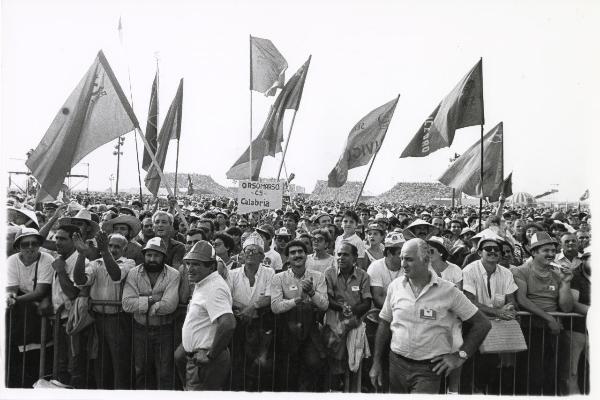 Ferrara - Festa nazionale de l'Unità 1985 - Aeroporto militare - Arena - Manifestazione di chiusura - Scorcio di una parte della folla che assiste al discorso di chiusura - Ritratto di gruppo - Bandiere - Cartello