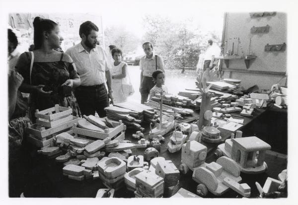 Milano - Festa provinciale de l'Unità 1985 - Monte Stella - Stand dedicato ai giocattoli in legno - Un bambino osserva il banco - Visitatori - Ritratto di gruppo - Ritratto infantile