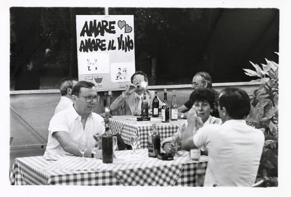 Milano - Festa provinciale de l'Unità 1985 - Monte Stella - L'enoteca - Gruppi di persone sedute ai tavoli degustano del vino - Cartello