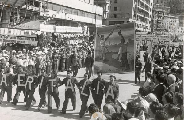 Genova - Festa nazionale de l'Unità 1950 - Sfilata per le vie della città - Spezzone di corteo con  gli operai della Aeritalia - Due volontari portano un grande manifesto illustrato - Striscioni - Bandiere