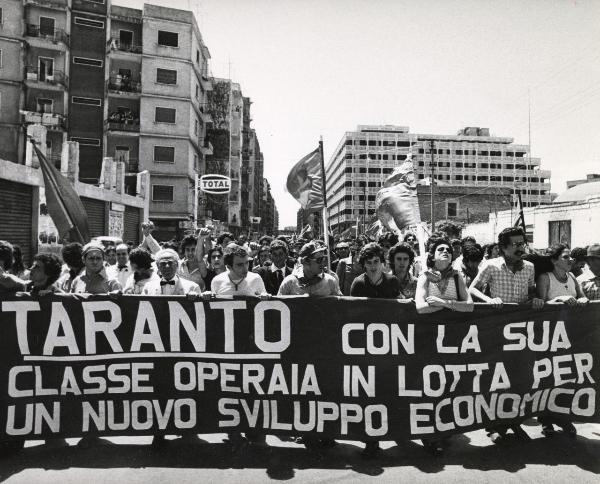 Bari - Festa nazionale d'apertura de l'Unità 1974 - Sfilata per le vie della città - Spezzone di corteo con  gli operai di Taranto che portano uno striscione - Bandiere - Cartelli