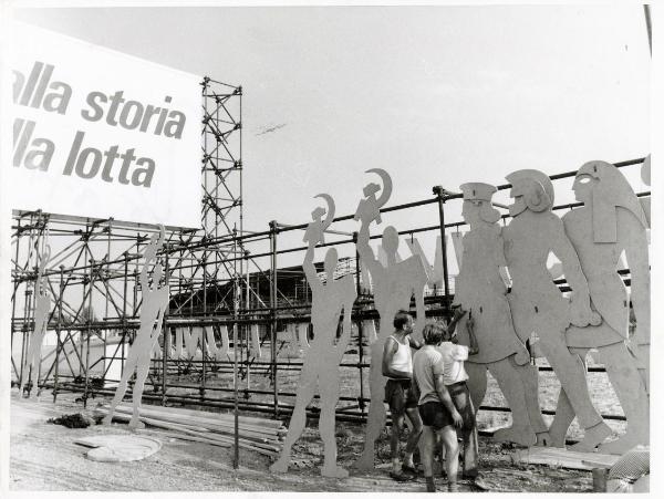 Bologna - Festa nazionale de l'Unità 1974 - Costruzione dell'ingresso principale - Operai al lavoro - Sagome metalliche - Cartello