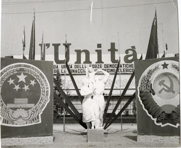 Modena - Festa nazionale de l'Unità 1957 - Piazza d'Armi - Spazio esterno con gruppo statuario e pannelli laterali con simboli della Cina e dell'Unione Sovietica - Scritta "Unità" su struttura metallica - Bandiere