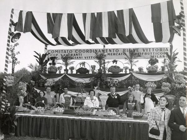 Milano - Festa nazionale de l'Unità 1958 - Parco Lambro - Stand del Comitato Coordinamento Rione Vittoria - Banco alimentare con esposizione di frutta - Cartelli - Bandiere - Ritratto di gruppo