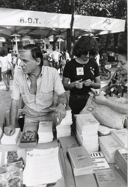 Milano - Festa nazionale de l'Unità 1979 - Parco Sempione - Stand della Repubblica Democratica Tedesca - Banco con libri e gadget - Addetti alla vendita - Ritratto