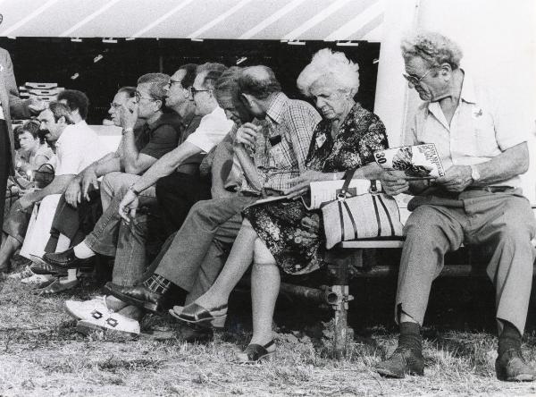 Bologna - Festa nazionale de l'Unità 1980 - Parco Nord - Un gruppo di visitatori si riposa su delle panche - Un uomo tiene in mano il programma della festa - Ritratto di gruppo