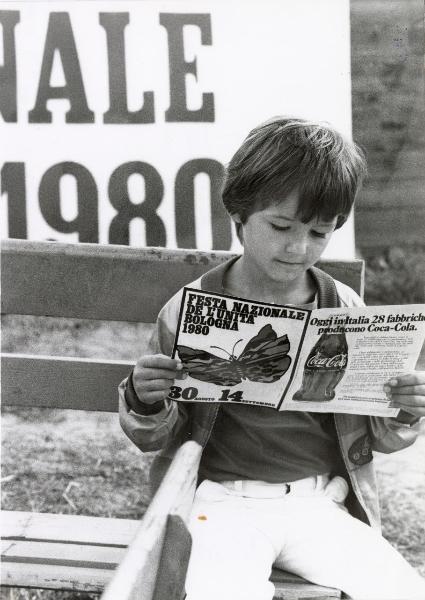 Bologna - Festa nazionale de l'Unità 1980 - Parco Nord - Un bambino seduto guarda il programma del festival - Ritratto infantile - Cartello