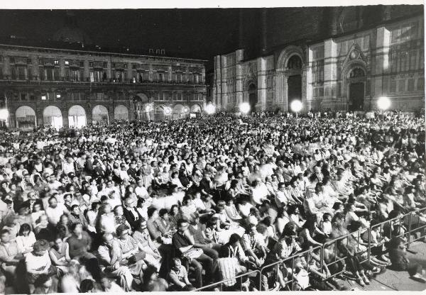 Bologna - Festa provinciale de l'Unità 1981 - Piazza Maggiore - Pubblico assiste a uno spettacolo - Veduta notturna - A sinistra facciata della basilica di San Petronio - Illuminazione - Architettura