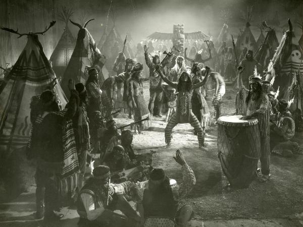 Scena del film "Il fanciullo del West" - Regia Ferroni, Giorgio, 1942 - Scena di un rito indiano in cui, al centro, un attore non identificato alza entrambe le braccia verso il cielo impugnando un'ascia. Intorno a lui, attori non identificati.