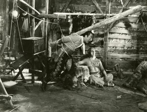 Scena del film "Il fanciullo del West" - Regia Ferroni, Giorgio, 1942 - Erminio Macario, in piedi al centro, è intento a muoversi verso destra, spostando un trabiccolo di funi e legna, che lo tiene prigioniero.