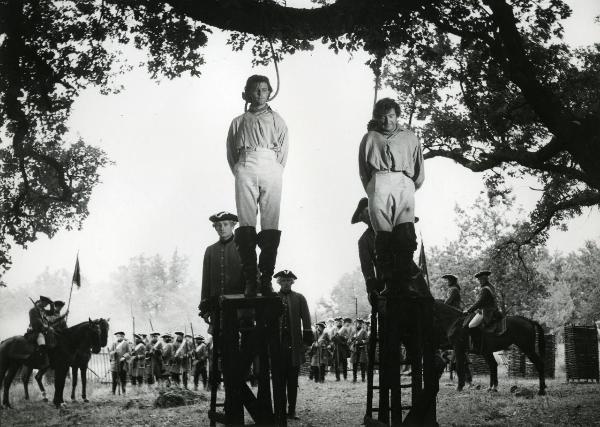 Scena del film "Fanfan la tulipe" - Regia Jacques, Christian, 1952 - Philipe Gérard, al centro, e un attore non identificato al suo fianco, sono in piedi sopra a degli sgabelli e hanno dei cappi al collo. Alle loro spalle attori non identificati.