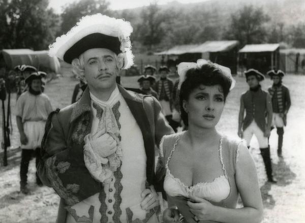 Scena del film "Fanfan la tulipe" - Regia Jacques, Christian, 1952 - In primo piano Gina Lollobrigida e un attore non identificato osservano davanti a loro. In secondo piano attori non identificati, in vesti militari, li osservano.