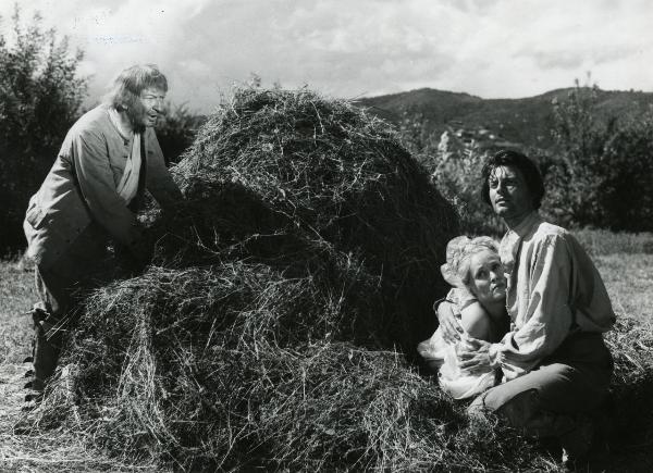 Scena del film "Fanfan la tulipe" - Regia Jacques, Christian, 1952 - A sinistra, un attore non identificato, appoggiato a un mucchio di fieno osserva Philipe Gérard e un'attrice non identificata che si stringono in un abbraccio.