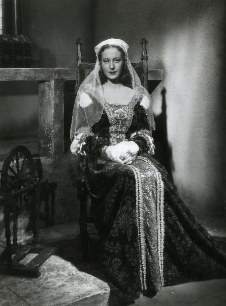 Scena del film "Fanfulla da Lodi" - Regia Duse, Carlo, Antamoro, Giulio, 1940 - Figura intera di Germana Paolieri, in abiti medioevali, seduta su una sedia con le mani giunte che rivolge lo sguardo verso l'obbiettivo.