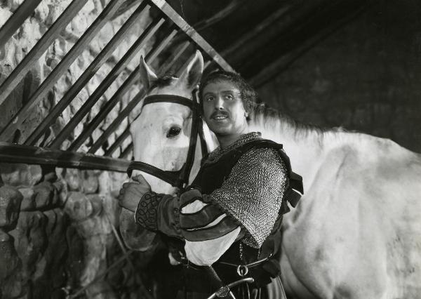 Scena del film "Fanfulla da Lodi" - Regia Duse, Carlo, Antamoro, Giulio, 1940 - Mezza figura di Ennio Cerlesi che, accarezzando il muso di un cavallo alla sua destra, rivolge uno sguardo sorridente verso destra.
