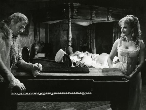 Scena del film "Fantasmi a Roma" - Regia Pietrangeli, Antonio, 1961 - In primo piano, Mastroianni appoggia la mano destra su un pianoforte e guarda in basso. Sandra Milo, a destra lo osserva. Dietro, distesi a letto, due attori non identificati.