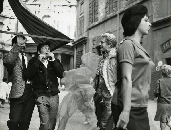 Scena del film "Fantasmi a Roma" - Regia Pietrangeli, Antonio, 1961 - In primo piano, un'attrice non identificata. Dietro, Marcello Mastroianni guarda sorridendo verso due attori non identificati. Uno di questi sta sbattendo la testa contro un'asta.