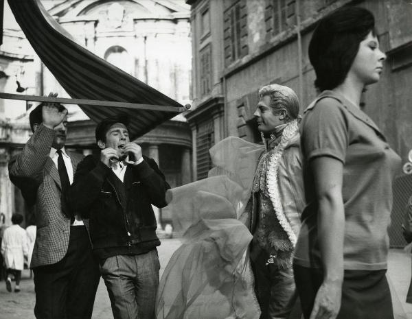 Scena del film "Fantasmi a Roma" - Regia Pietrangeli, Antonio, 1961 - In primo piano, un'attrice non identificata. Dietro, Marcello Mastroianni guarda sorridendo verso due attori non identificati. Uno di questi sta sbattendo la testa contro un'asta.