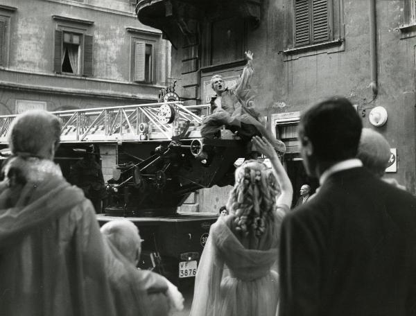 Scena del film "Fantasmi a Roma" - Regia Pietrangeli, Antonio, 1961 - Vittorio Gassman, seduto su un furgone dei pompieri, fa un cenno di saluto a degli attori non identificati in primo piano.
