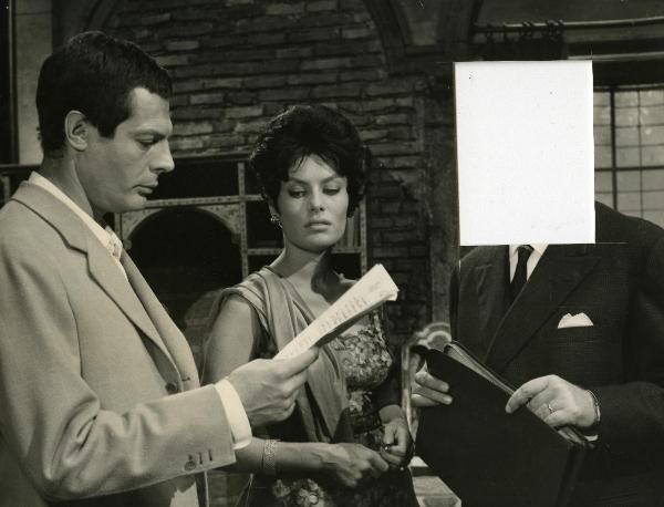 Scena del film "Fantasmi a Roma" - Regia Pietrangeli, Antonio, 1961 - Mastroianni, a sinistra, legge un documento. Intanto, Belinda Lee, al centro guarda in basso e un attore non identificato a destra tiene in mano un porta documenti.