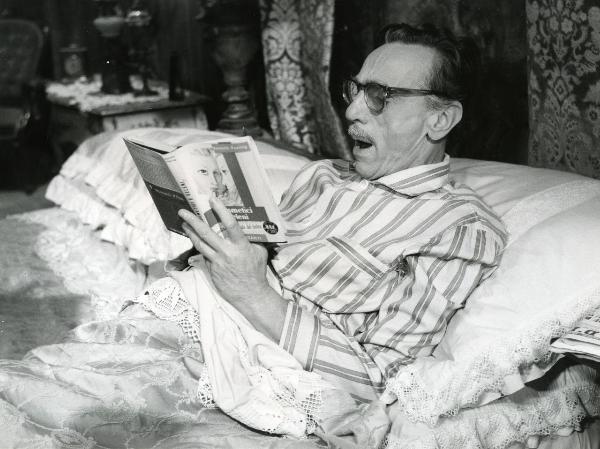 Scena del film "Fantasmi a Roma" - Regia Pietrangeli, Antonio, 1961 - Eduardo De Filippo, steso a letto con la schiena sollevata da un cuscino, sbadiglia, mentre è intento nella lettura del libro "Cosmetici e veleni".
